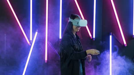 young woman playing shooter game in the virtual reality. virtual reality helmet on color lighting smoke background