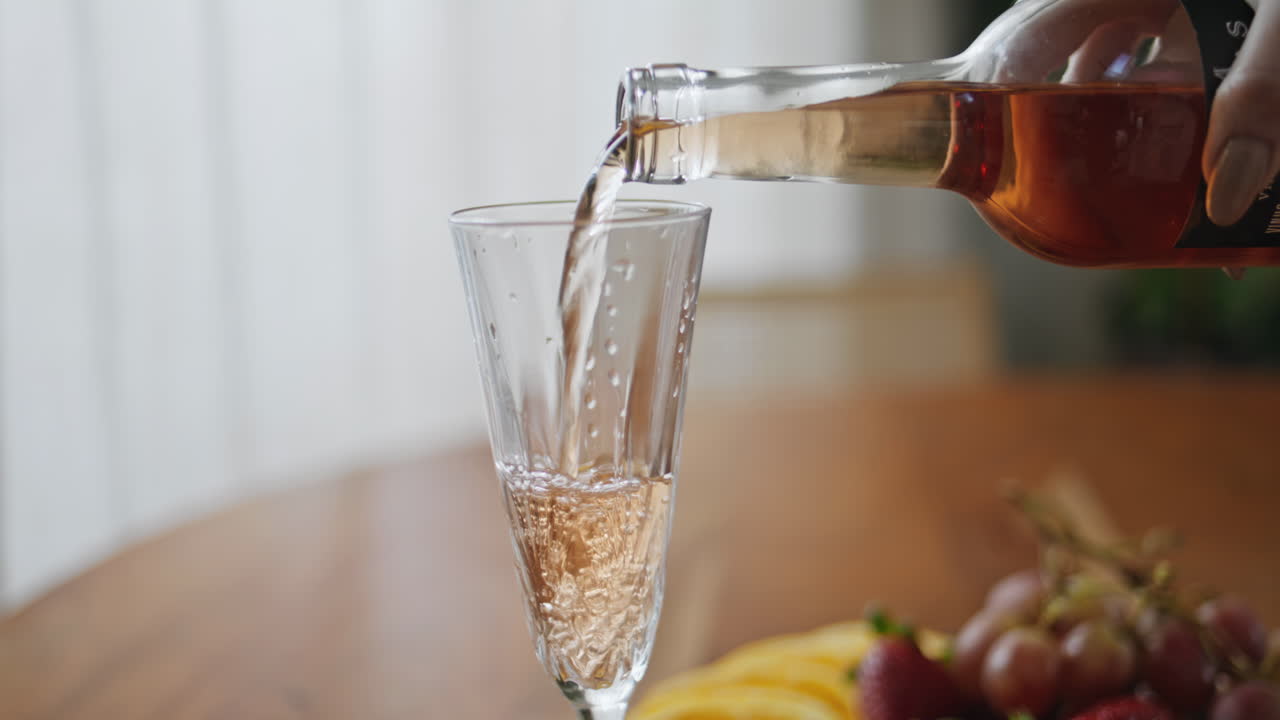 Closeup pouring wine glass on wooden table. Woman hand holding alcohol bottle
