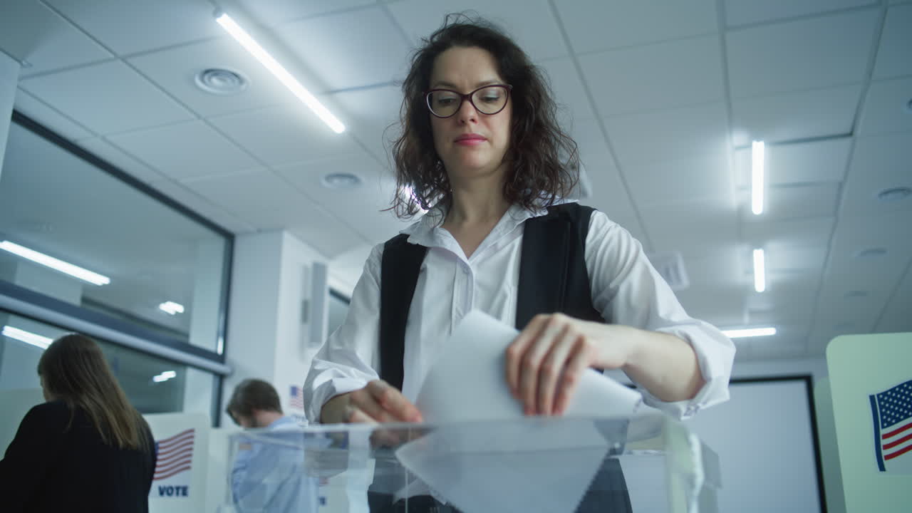 Caucasian Female Voter Puts Bulletin in Box after Voting Caucasian Female Voter Puts Bulletin in Box Diverse People American Citizens Vote for Future President in Voting Booths at Polling Station Elections Day in the United States of America Democracy