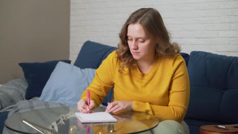 woman is writing something on sheets of paper at glass table with pen. she reads something and corrects it with pen. studying something, preparing for speech, checking contract, training, lecture