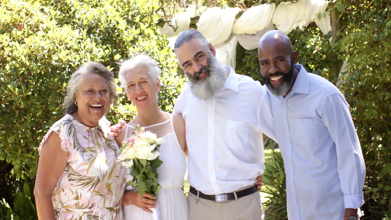 Smiling senior friends posing together at outdoor wedding, holding bouquet