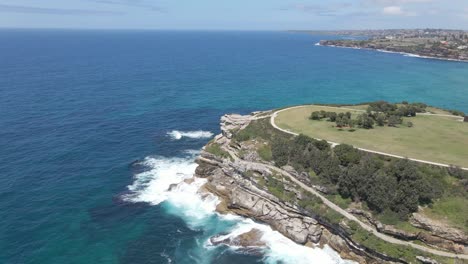 waves hitting rocky cliffs with coastal walk at mackenzies point peninsula - tamarama in nsw, australia