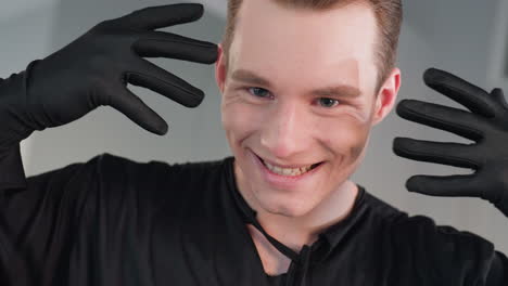 close up of young man in black gloves playfully covering face then revealing expression in bright mirrored studio, capturing dynamic gesture and playful mood with sharp focus on eyes and hands