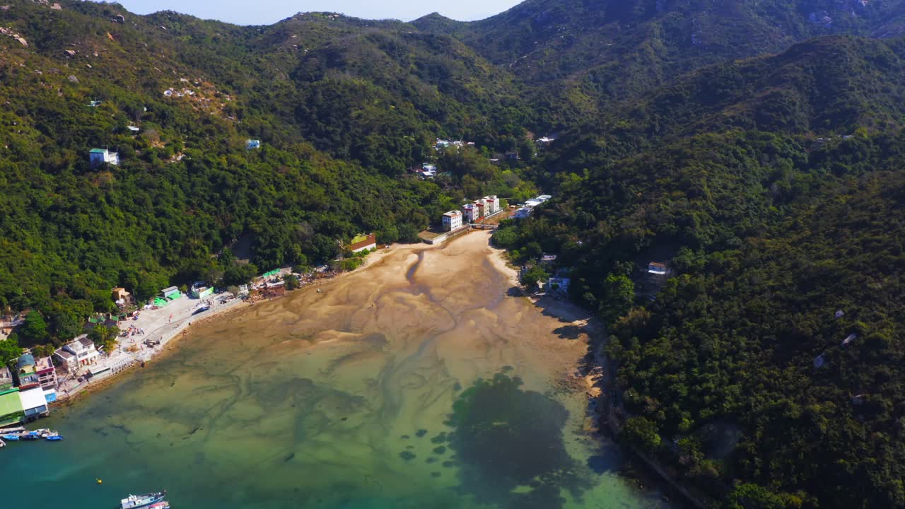 낮 동안 모래 진흙이 있는 아름다운 작은 강 삼각주를 향해 부두와 굴 양식장이 있는 작은 어촌 위로 앞으로 이동하는 드론 샷