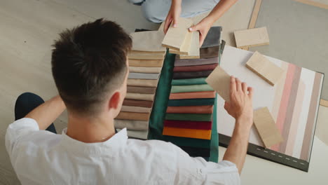 a young couple picks up fabric and wallpaper to repair their home. compare samples of wood, fabric and wallpaper