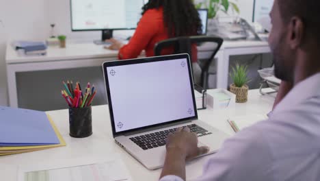 feliz hombre de negocios afroamericano sentado en un escritorio, usando una computadora portátil con espacio de copia en una oficina moderna