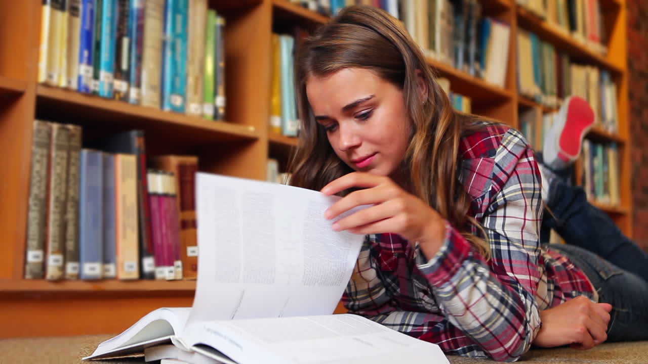 Studente sdraiato per terra che legge in biblioteca