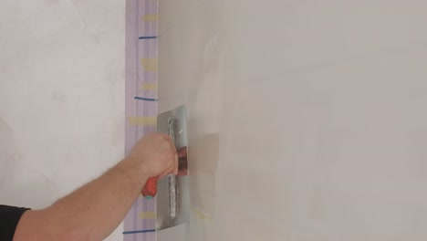 man plastering the walls with finishing putty in room with putty spatula