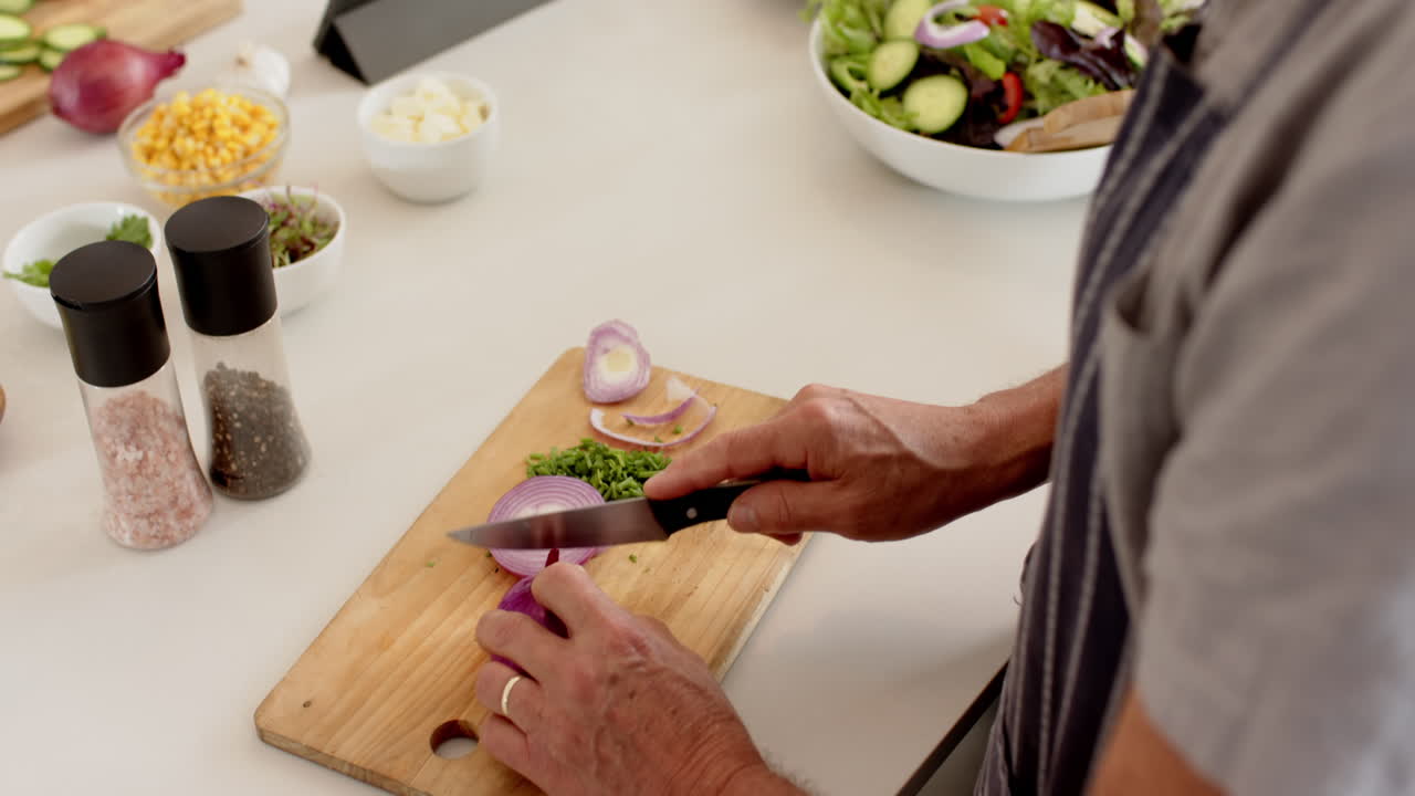 Chopping onions on cutting board, senior preparing fresh salad in kitchen