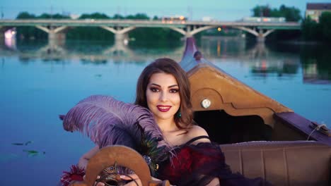 a charming woman with a bright make-up is holding a violet feather in her hand and smiling in the evening on the gondola. blurred background