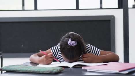 in a school classroom, a young biracial girl concentrates on her workbook