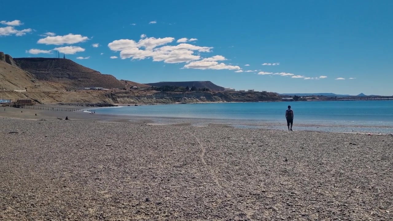Un uomo solitario cammina lungo l'interminabile litorale di Comodoro Rivadavia, Argentina, vivendo la pacifica vastità della Patagonia. Bassa marea, cieli blu e l'Oceano Atlantico.