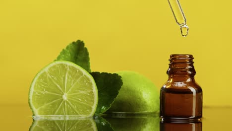 dripping oil from pipette into bottle close-up, lime juice. making aroma serum on yellow background. dropping liquid citrus extract, skincare routine, treatment spa concept. traditional medicine