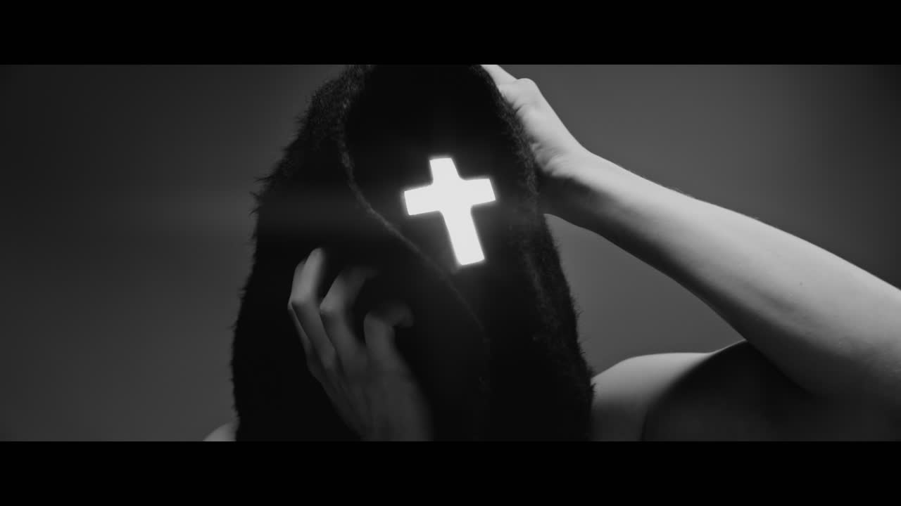 Masked man with cross of light glowing on his face grabs his head with his hand