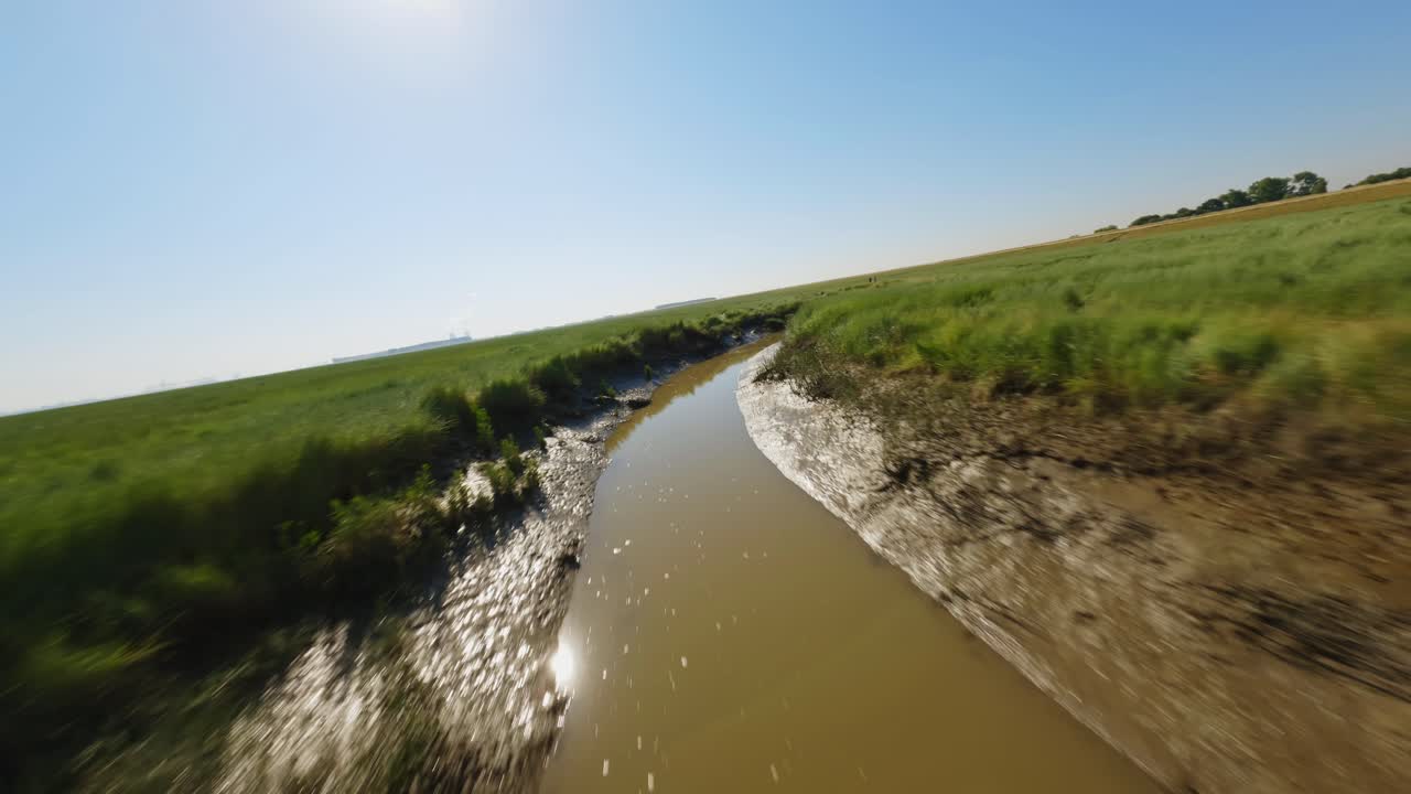 fpv drone shot rastreando una zanja fangosa que serpentea a través de hermosos humedales verdes en zelanda, los países bajos, en un día soleado de verano