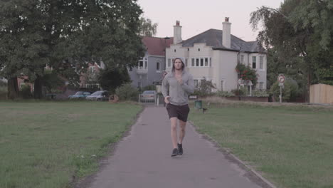 young athletic man goes for a run in the park, runs towards camera in slow motion - ungraded