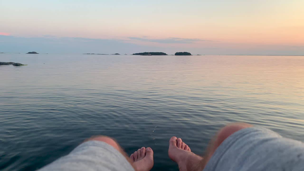 석양에 잔잔한 바다 위에 다리를 매달고 있는 남자