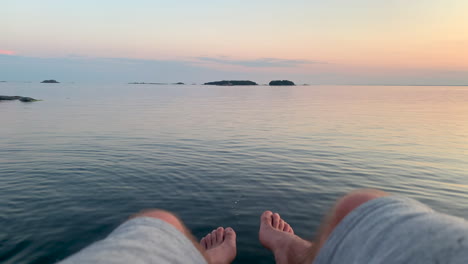 hombre colgando sus piernas sobre el mar en calma al atardecer