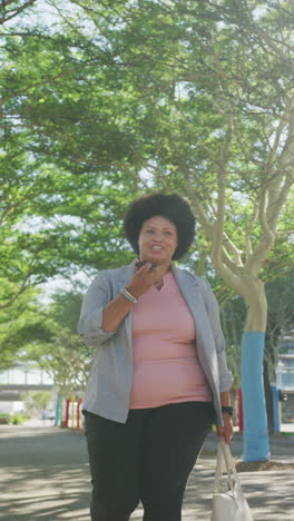 vertical video of happy plus size biracial woman using smartphone and walking on street