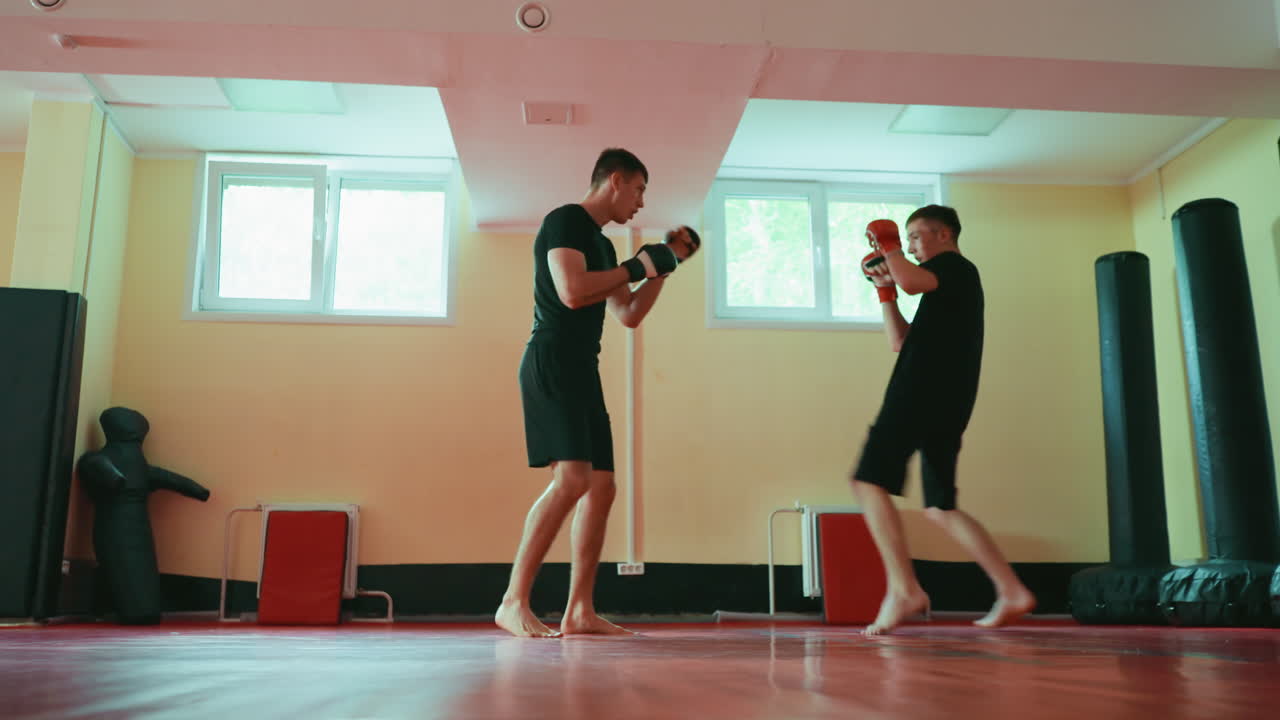 Two fighters sparring in gym on red mat, barefoot, wearing gloves, facing each other in combat stance, practicing martial arts techniques, focusing on agility, endurance, strength,fighting under natural light