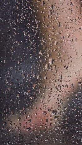 blurred young woman feet behind shower cabin misted glass with hot water drops flowing down daily hygiene routine slow motion extreme closeup
