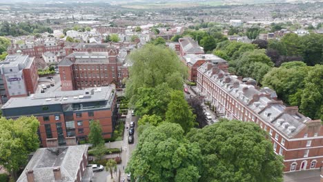 Scenic-aerial-flyover-of-Southernhay-Square-in-Exeter,-Devon,-showcasing-the-harmonious-blend-of-historic-and-modern-architecture-amidst-lush-greenery