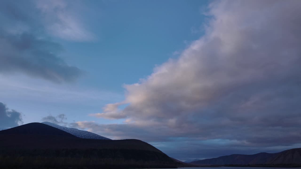 Witness the mesmerizing transformation of clouds as they glide overhead, casting shadows on the serene mountain landscape during the twilight hours.
