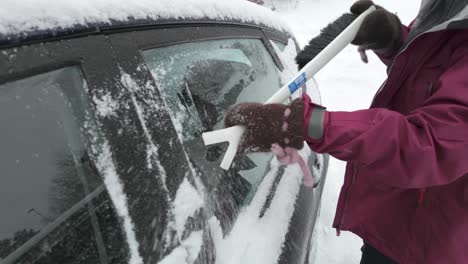 a hand scraping ice off the surface of the car - close up