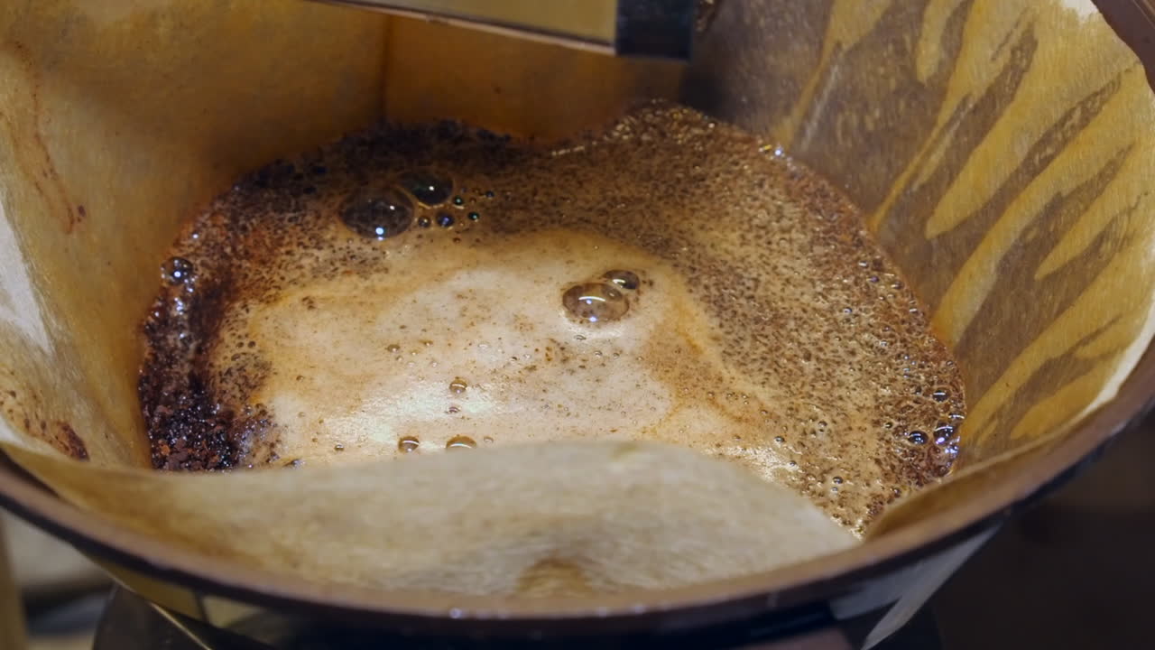 Close up view: Water drips into filter of brown coffee grounds on pot