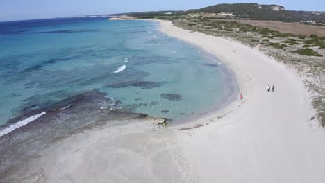 personas caminando en el sol de mediodía a lo largo de la playa de son bou en menorca, españa
