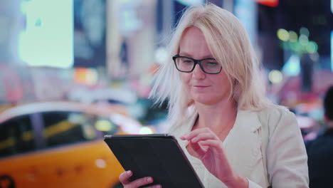 a woman uses a tablet on the street of manhattan behind her pass the famous yellow cabs - the symbol