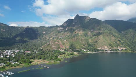 vista de avión no tripulado en guatemala volando sobre un lago azul rodeado de montañas verdes y volcanes en un día soleado en aitlan