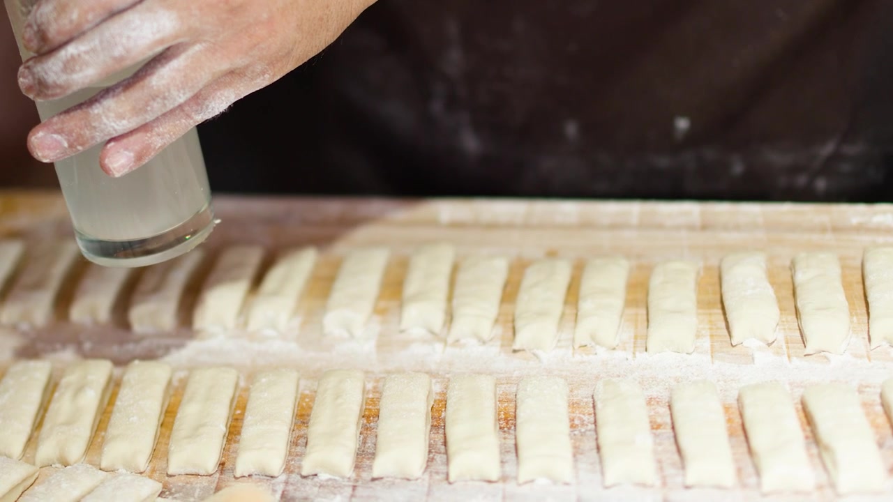 Close-up of hands using water glass to press dough strips for traditional street food.