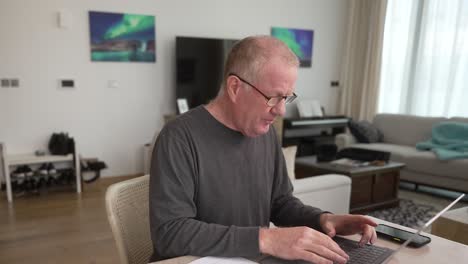 frustrated senior man trying to fill out forms and organize paperwork on a laptop computer