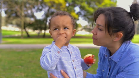 mixed-race pretty mother looking at son eating apple