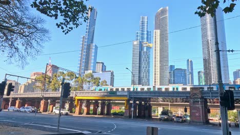 train passes under bridge with city backdrop