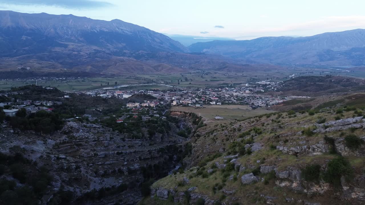 vuelo de avión no tripulado: volando a través del paso montañoso albanés al paisaje urbano con majestuosas montañas en el horizonte