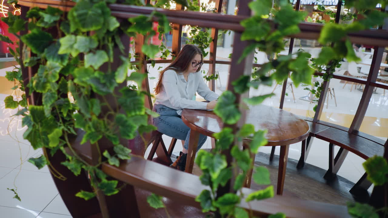 장식 된 나무 좌석에서 전화에 초점을 맞추고, 그녀의 에 쇼핑 가방, 배경에서 는 사람과 함께, 활기찬 쇼핑몰 내부의 활기찬 레스토랑 설정