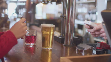 Close-Up-Of-Female-Customer-In-Bar-Making-Contactless-Payment-For-Drinks-In-Health-Pandemic