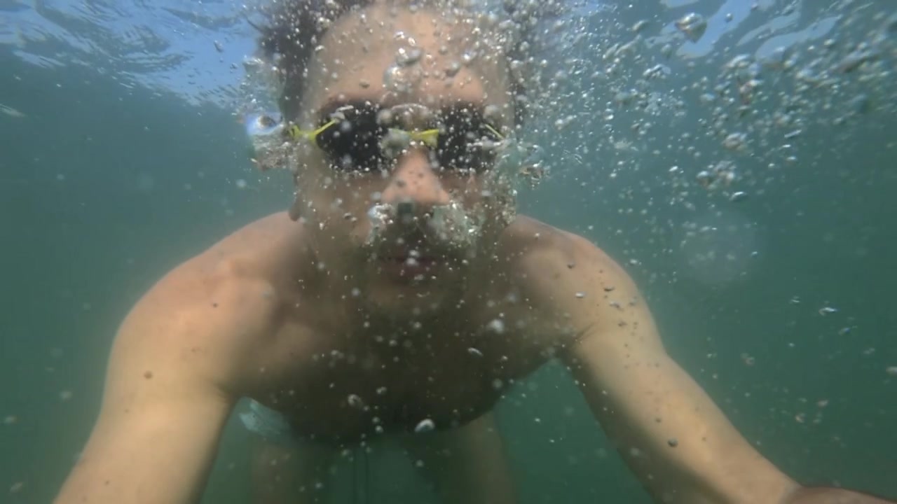 Uomo che si gode le vacanze estive sott'acqua, creando bolle, guardando direttamente la fotocamera, provando libertà ed esplorazione.