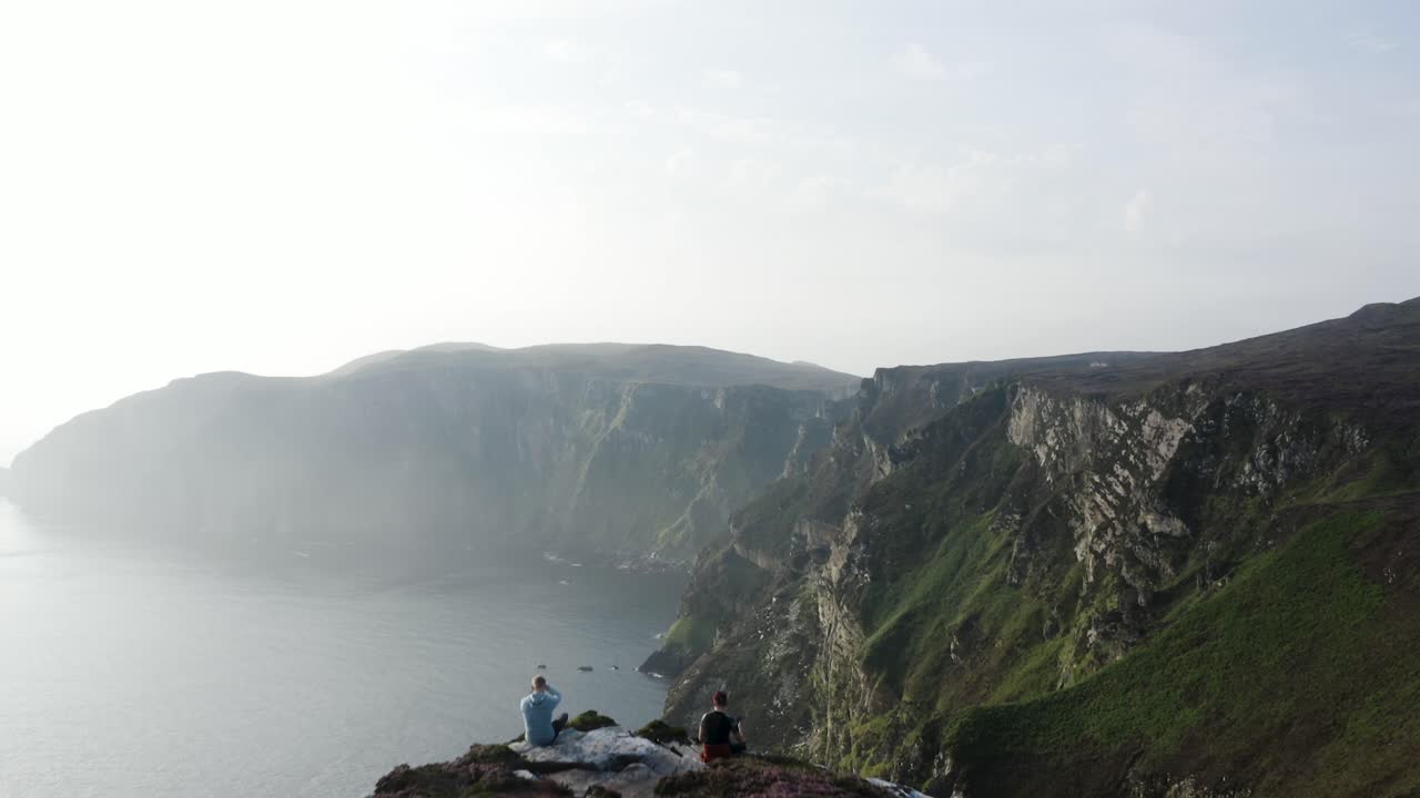 İrlanda'nın Donegal bölgesindeki Horn Head'de uçurumda oturup dağ silsilesine bakan iki kişi