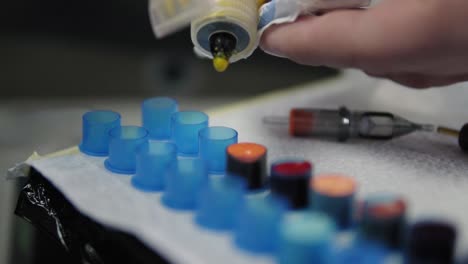 slow motion footage of tattoo master dropping yellow ink into the containers. professional tattoo master filling the cups with ink for working process. close up