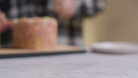 defocused shot of person at home cutting slice from rainbow celebration cake on table