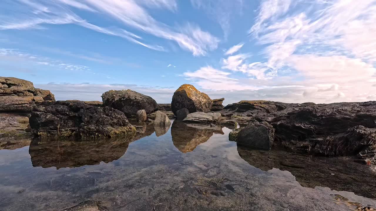 Zrcadlový odraz skalního útvaru na pláži v čisté mořské vodě pod dokonalou modrou tropickou oblohou.