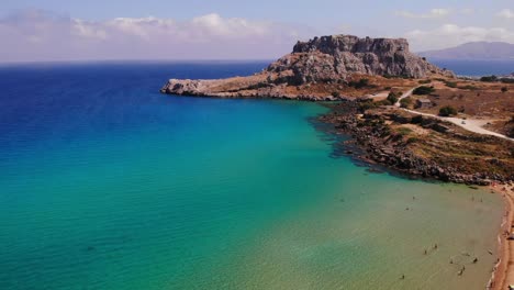 Tourists-In-The-Mediterranean-Sea-With-Rocky-Headland-In-Rhodos-Island-Beach,-Greece