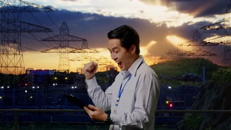 side view of an asian male professional worker standing with his tablet near high voltage tower, industrial facility, he raises his fist up with screaming goal after check on the tablet