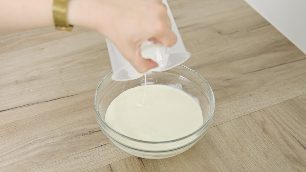 Vertical clip of cream being poured into a clear bowl for tiramisu recipe step