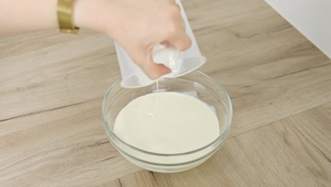 vertical clip of cream being poured into a clear bowl for tiramisu recipe step