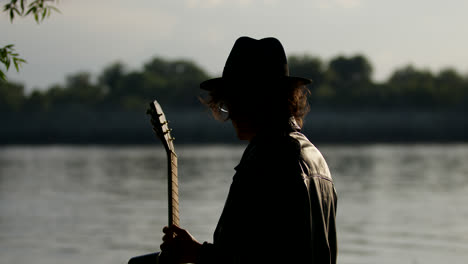 man playing guitar by the river at sunset