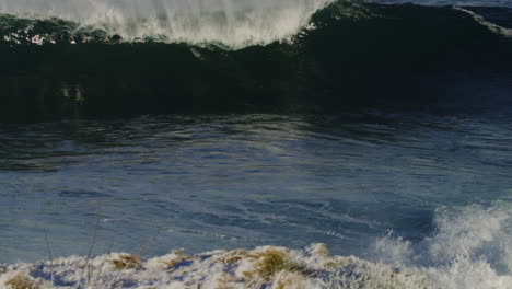 powerful wave swallows up surfers in wetsuits exploding into whitewash, slow motion viewed from above snow covered cliff